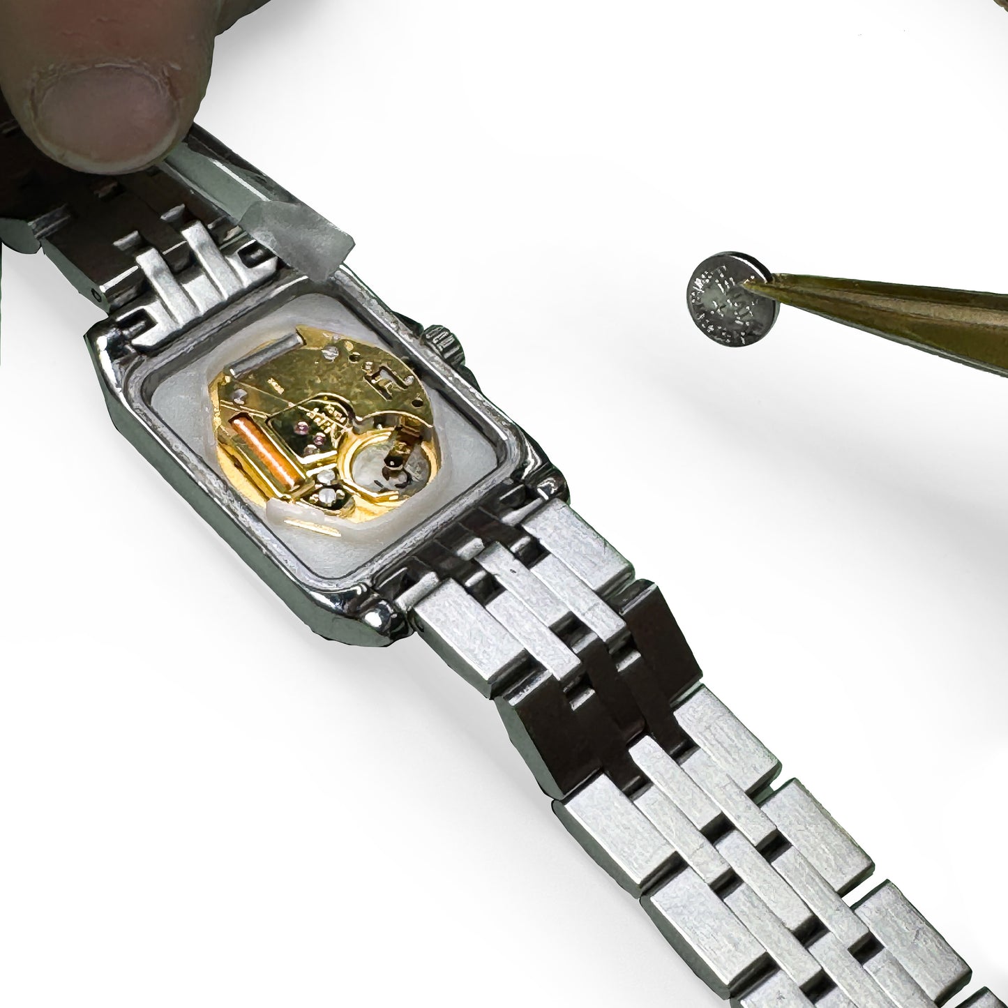 Close-up of a silver watch with a visible mechanical movement and battery shown being replaced on a white background